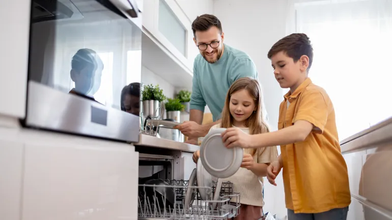 En pappa och två barn ställer smutsig disk i diskmaskinen.