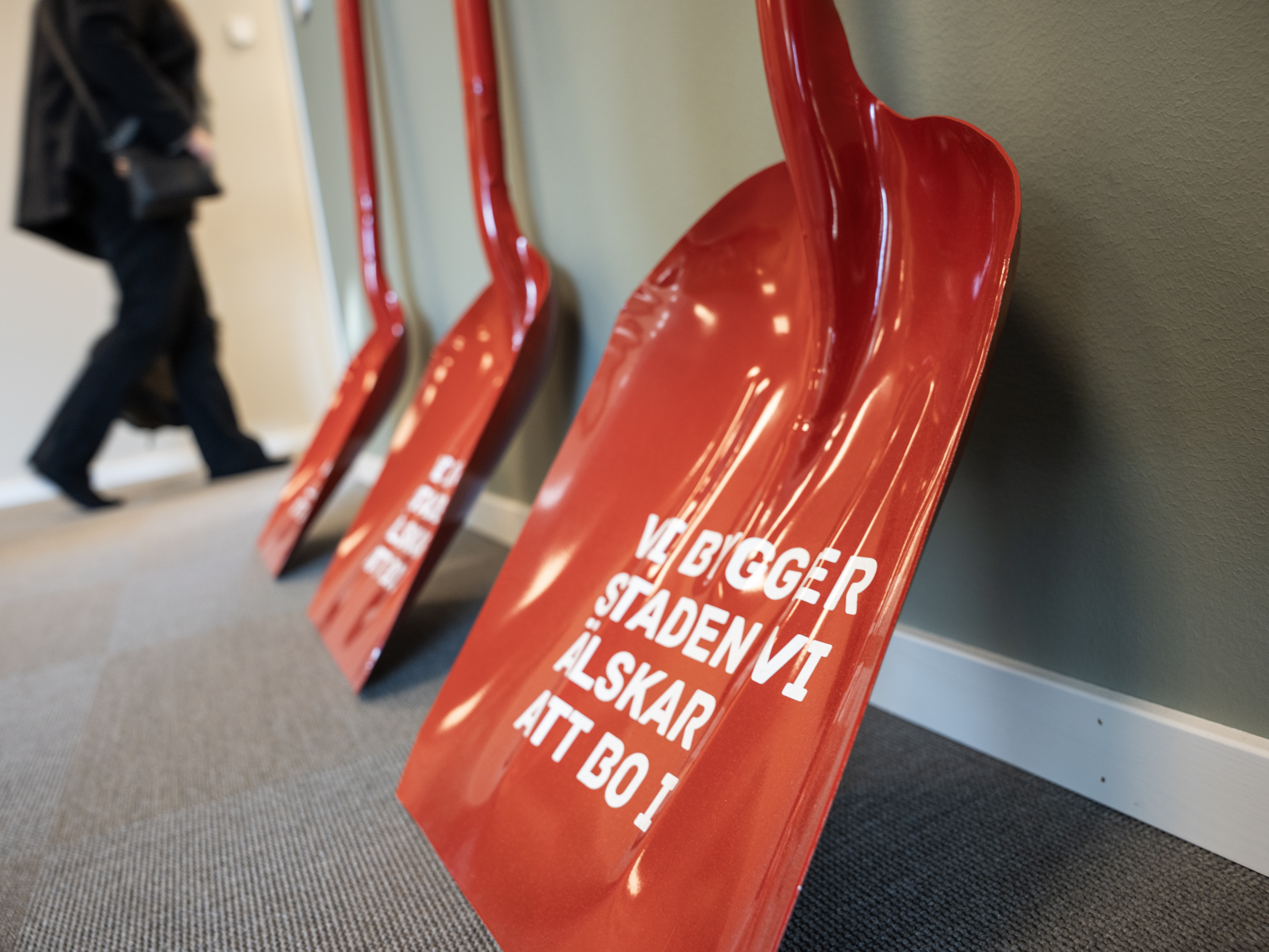 Tre röda spadar på rad med Tuna Entreprenads slogan "vi bygger staden vi älskar att bo i" i vit färg på spadarna.