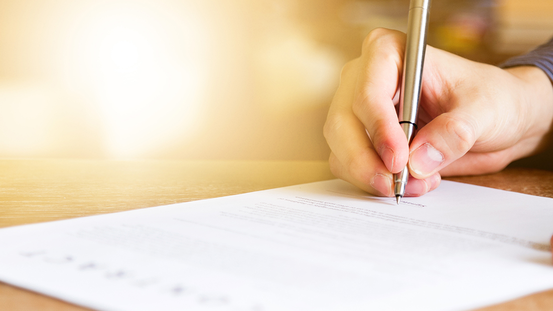 En hand håller i en penna över ett papper.