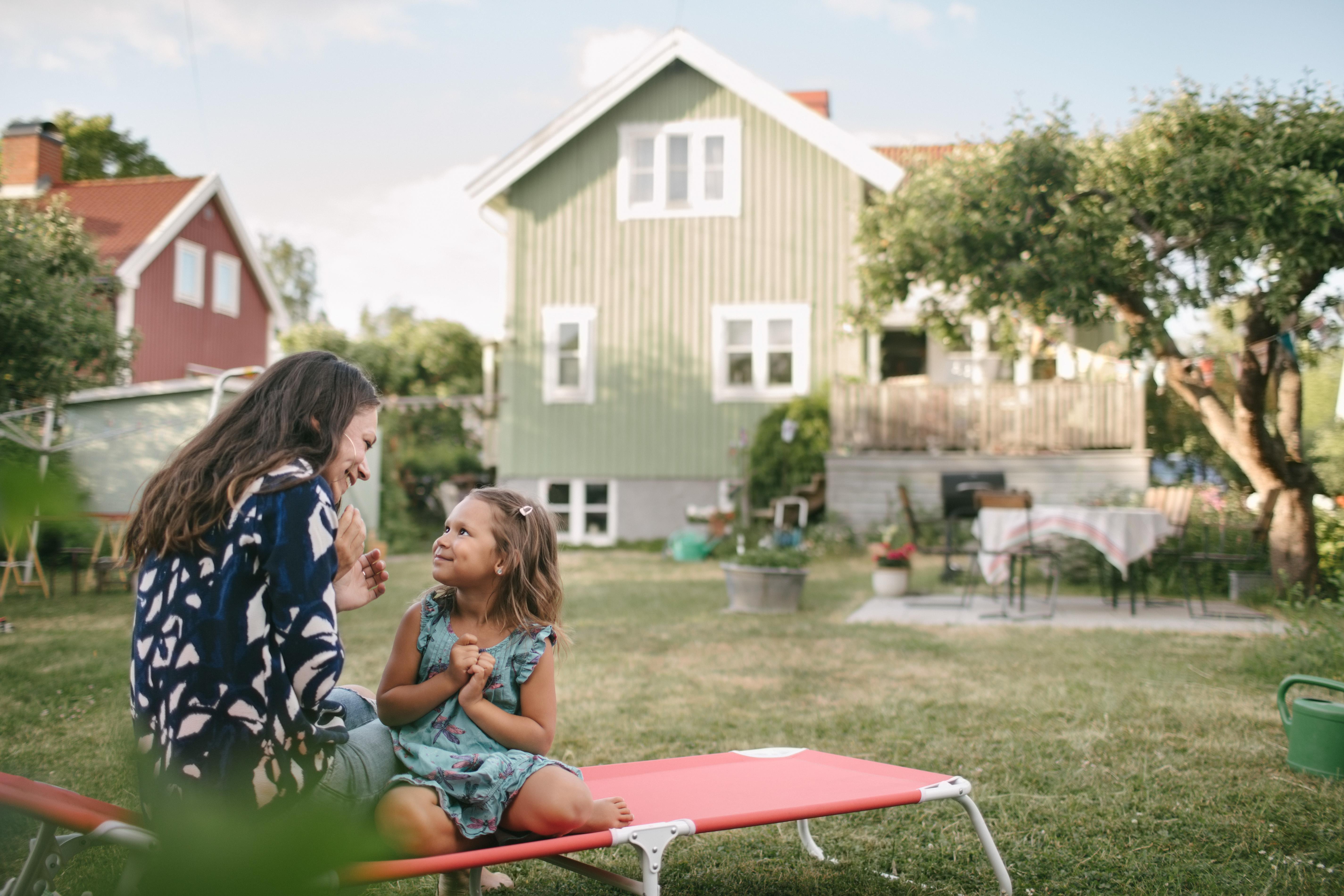 Mor och dotter sitter på en solstol i trädgården.
