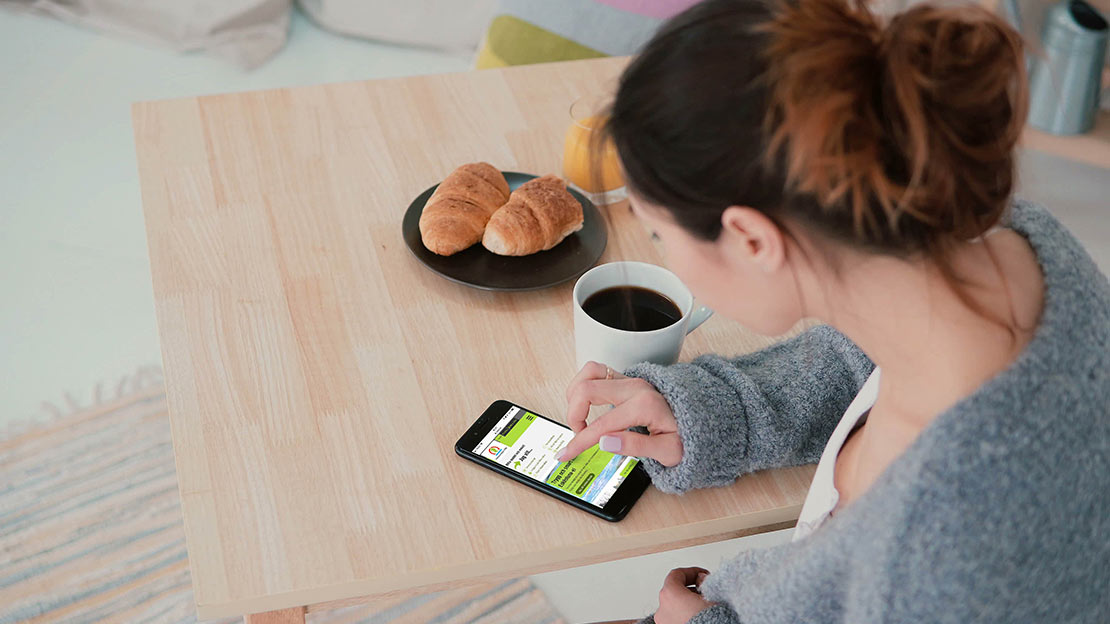 En kvinna skrollar på en mobil på ett bord.