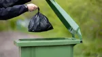 Person slänger svart påse i sopkärl.