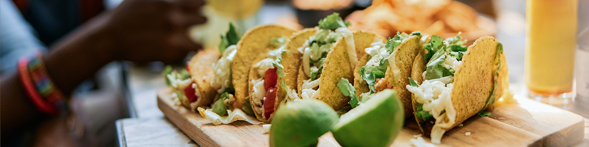 Flera färdiga tacos på en bricka tillsammans med lime med människor i bakgrunden som har trevlig tillsammans.
