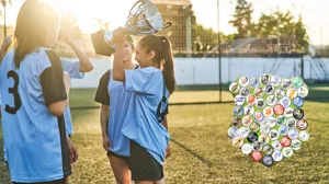 Barn iklädda fotbollströjor står på en gräsmatta och håller i en pokal
