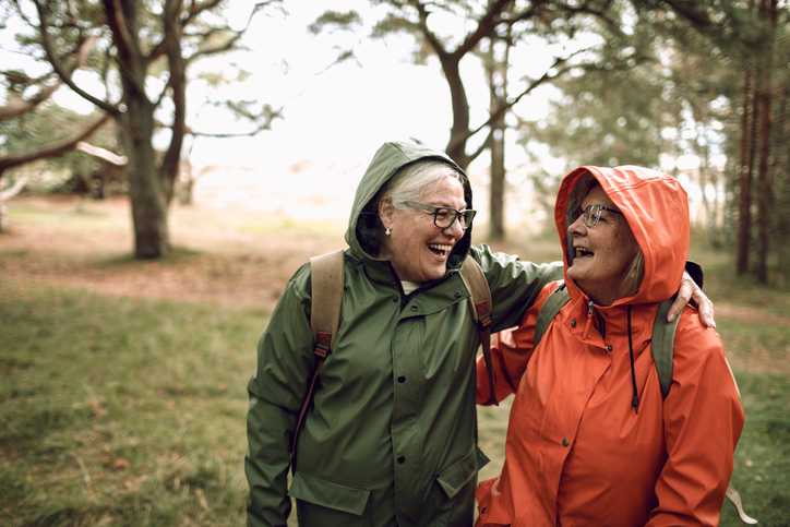 Två kvinnliga väninnor i regnjackor i skogen som omfamnar varandra