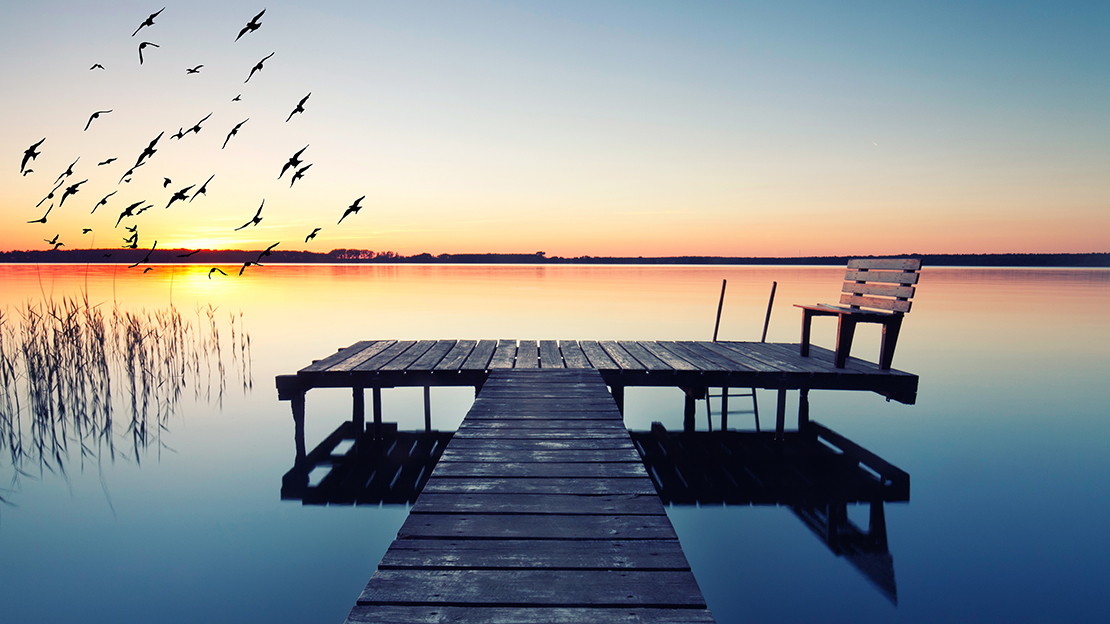 Brygga vid stilla sjö i solnedgång.