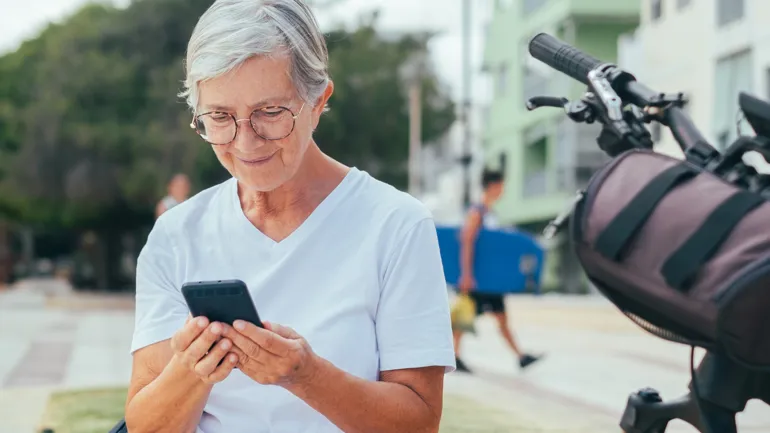 Äldre kvinna sittandes utomhus med en mobil.