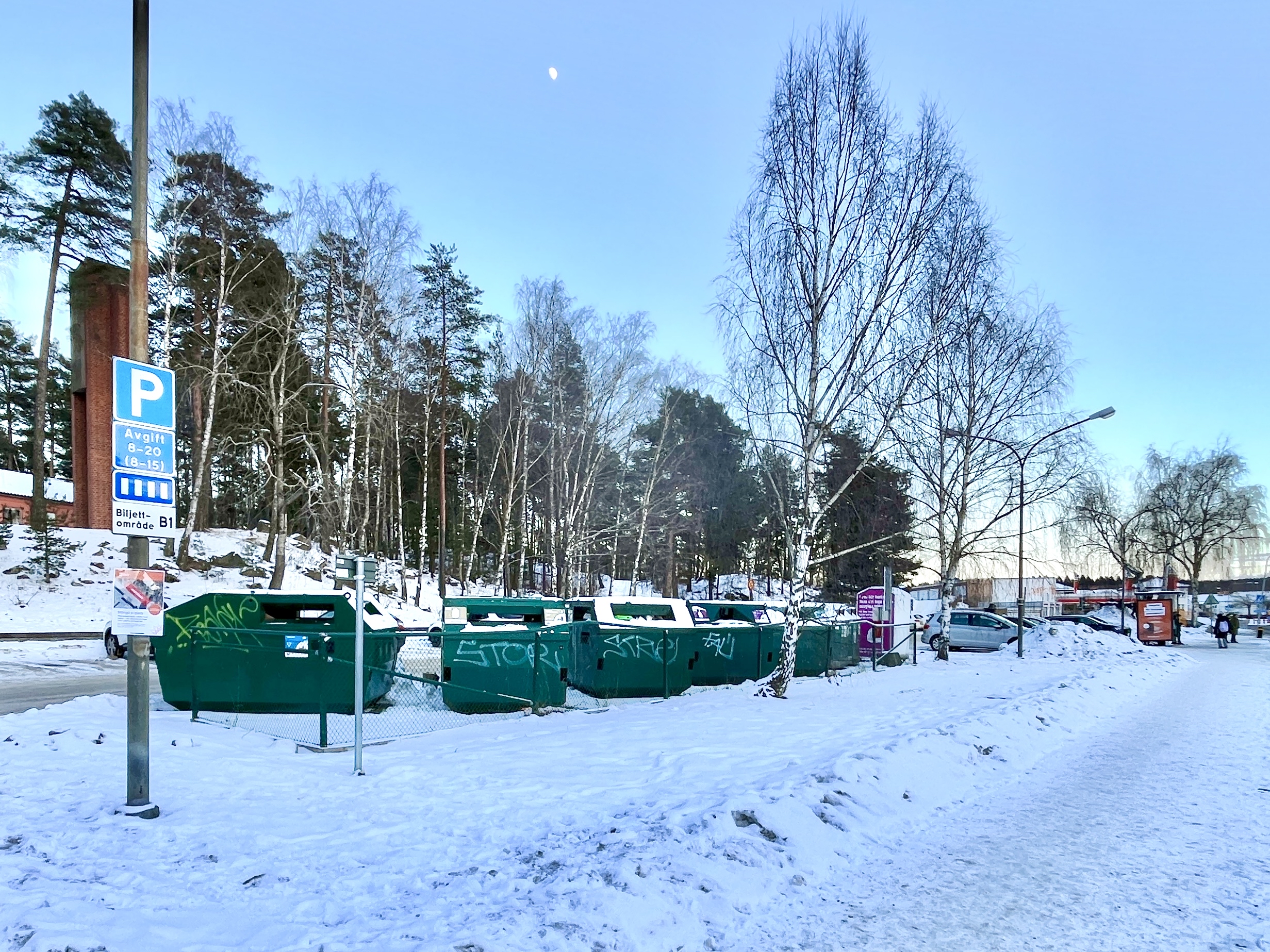 Återvinningsstation där flera containrar står på rad i snön.