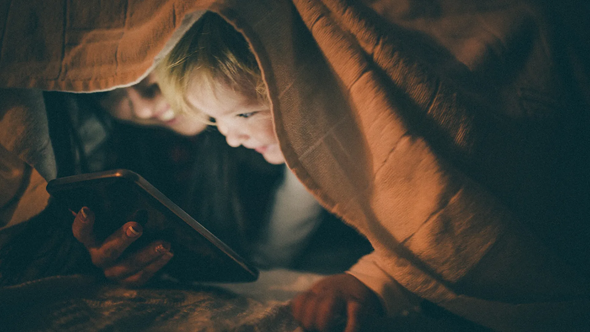 En kvinna och ett barn tittar fram under en filt och tittar i en mobil
