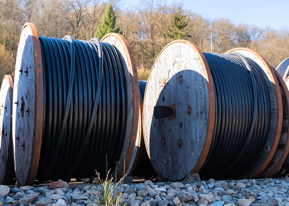 Flera stora kabeltrummor med svart kabel placerade på marken utomhus.