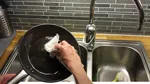 En hand torkar ur fettet från stekpannan.