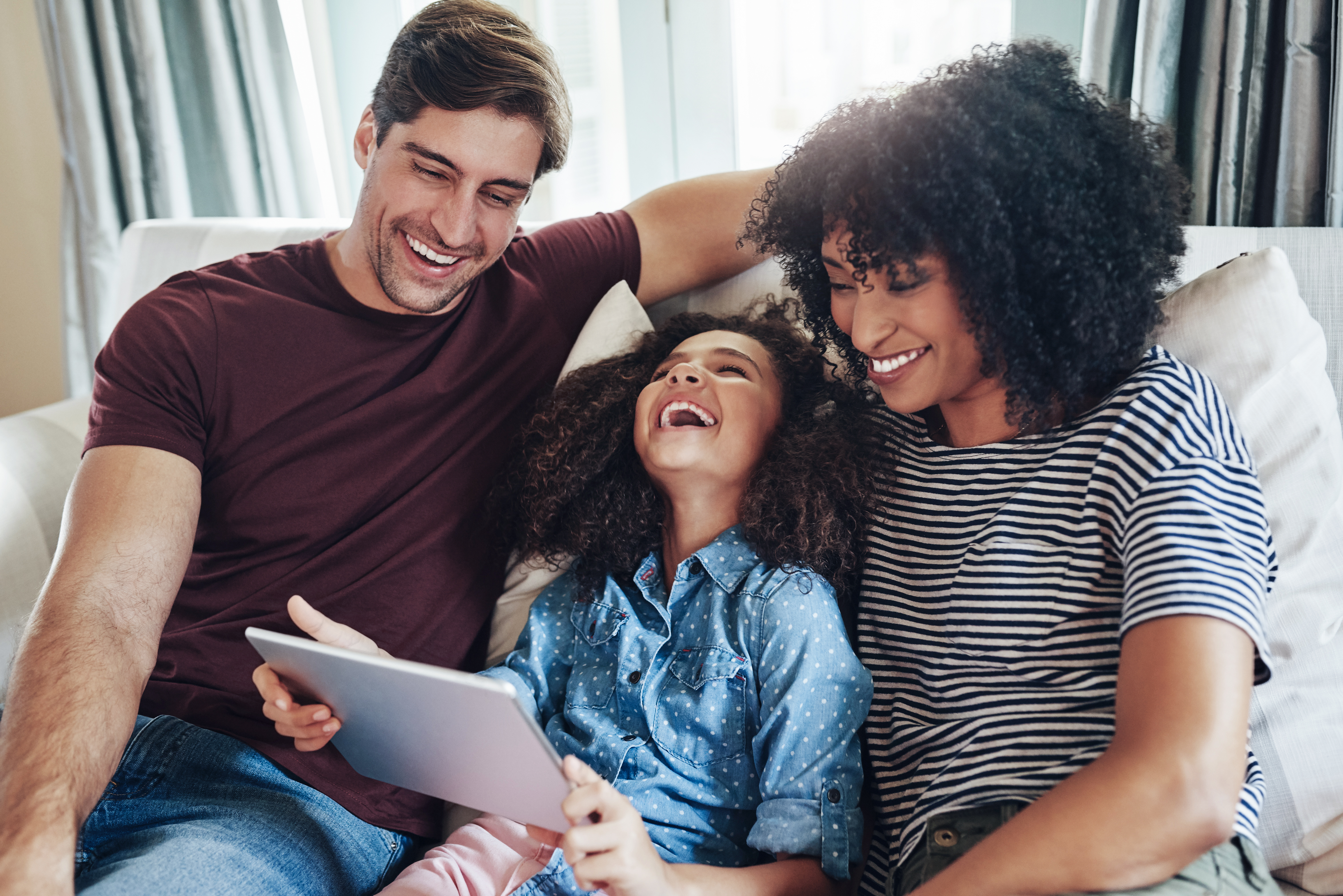 En familj som sitter i soffan och skrattar åt någonting som visas på en iPad.