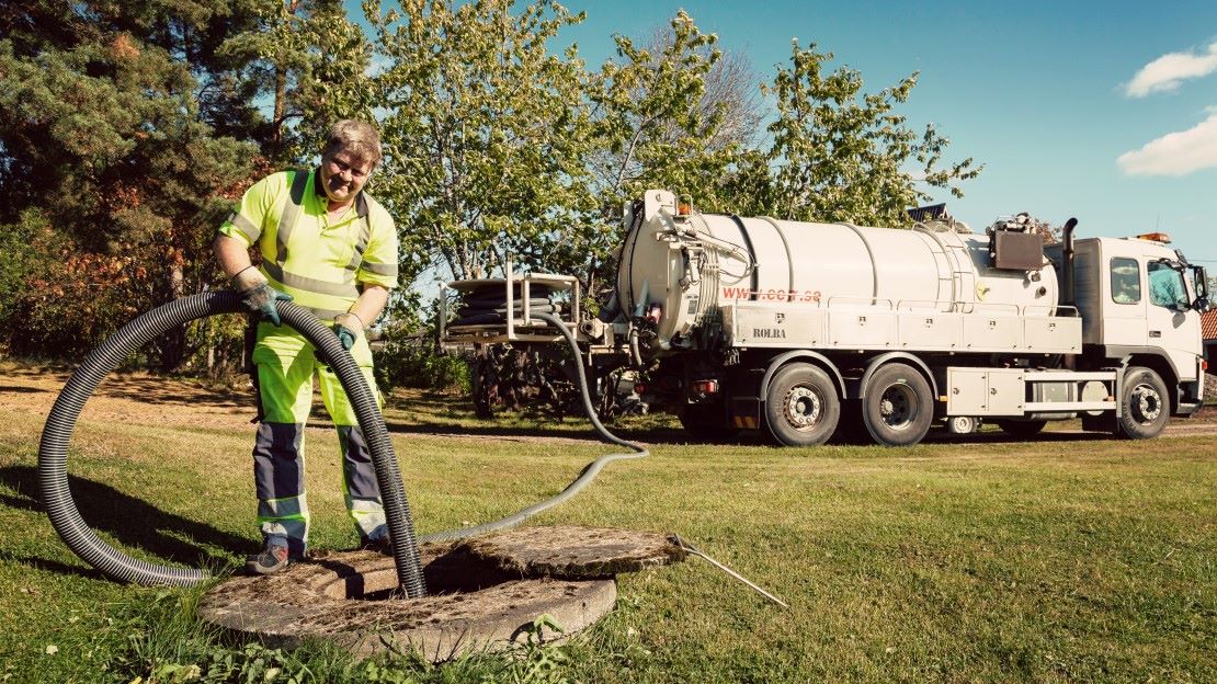 En slamtömningsbil och en man som tömmer en slambrunn.